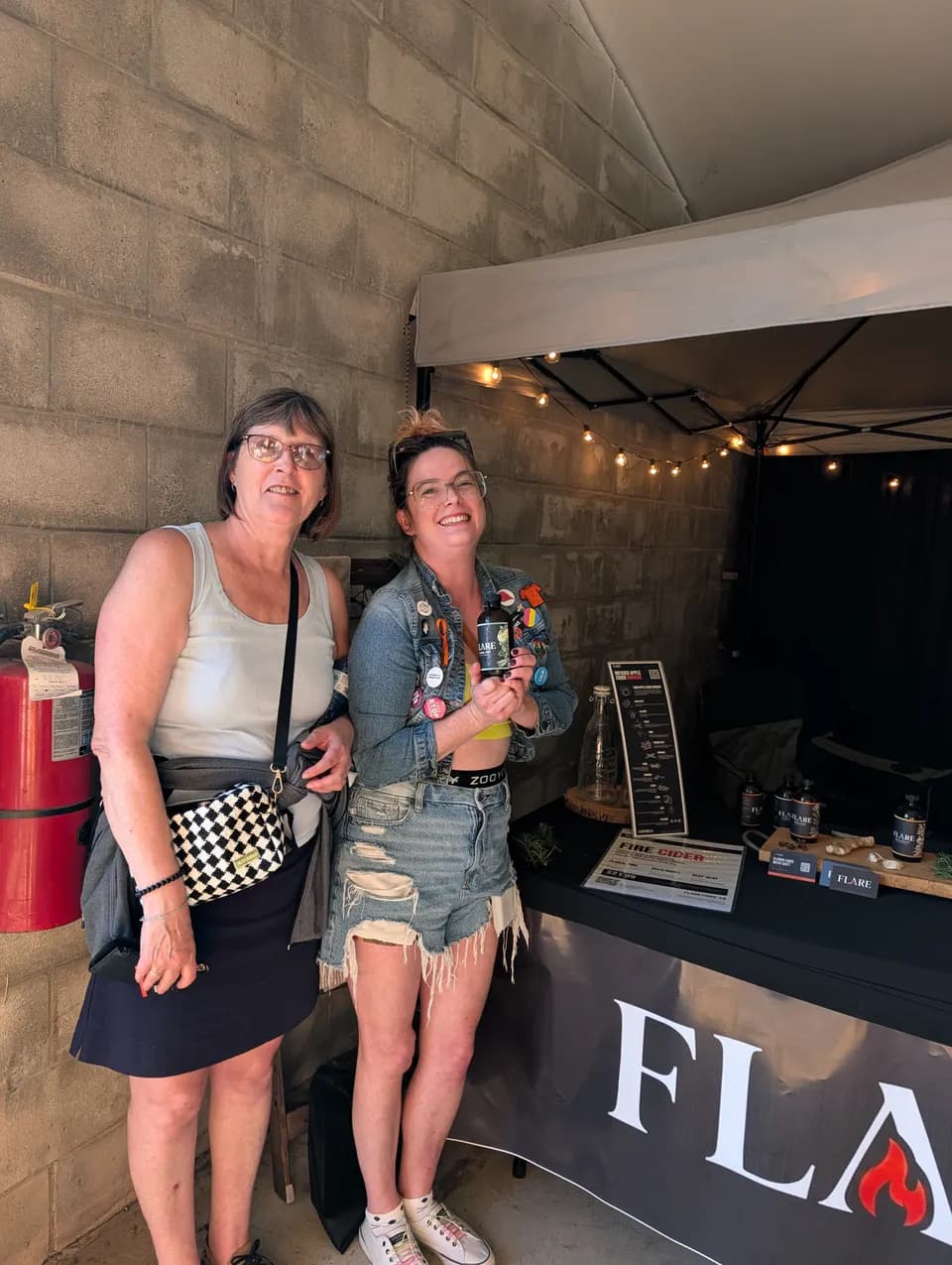 Two women stand at the stall, the younger one holding a bottle of Flare in both hands.