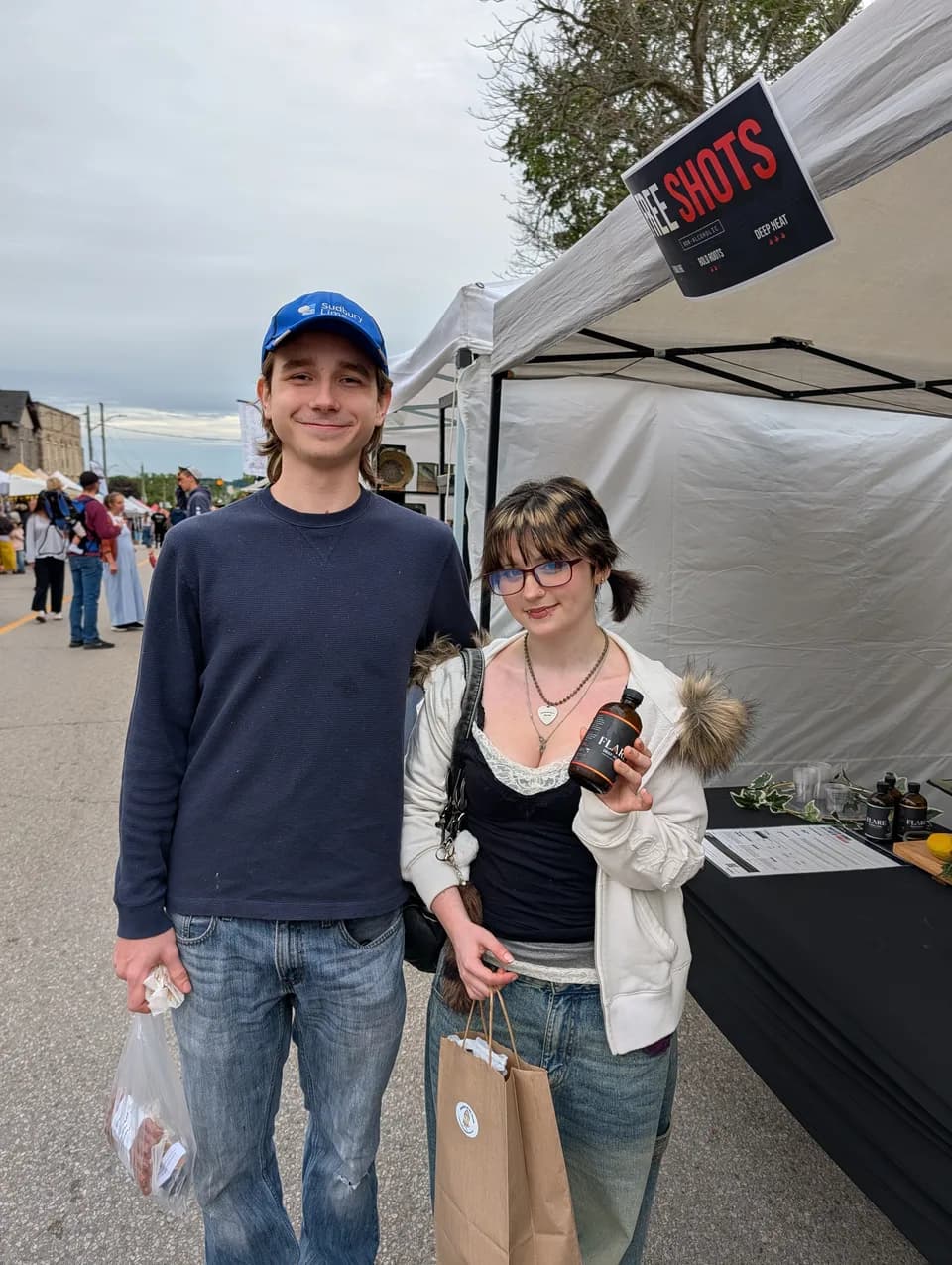 A young couple at the Flare stall on a busy street, she holding up a bottle of Flare, he in a blue cap.